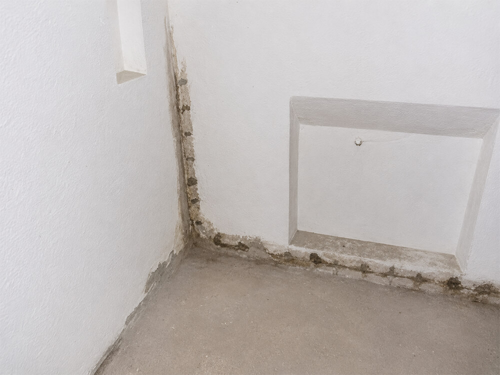 Ein leerer Raum mit weißen Wänden und einem sichtbaren Mauerwerk in der Ecke, der eine minimalistische Atmosphäre ausstrahlt.